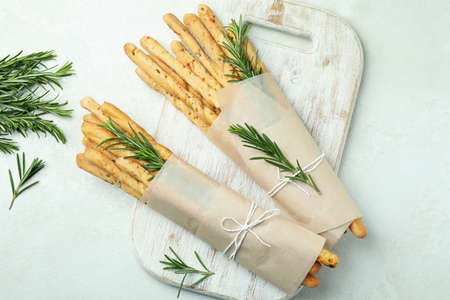 Board with tasty grissini on white textured background