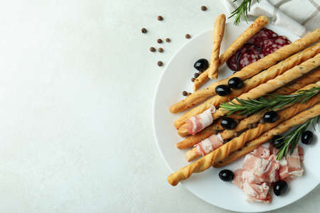 Plate with grissini and snacks on white textured background