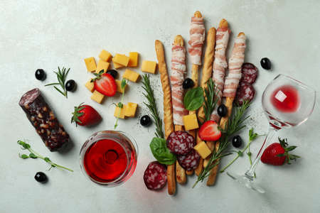 Grissini sticks with bacon, snacks and wine on white textured background