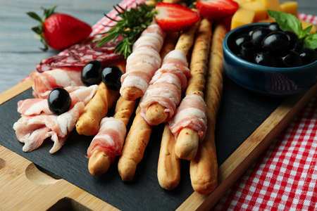 Board with grissini and snacks on wooden background