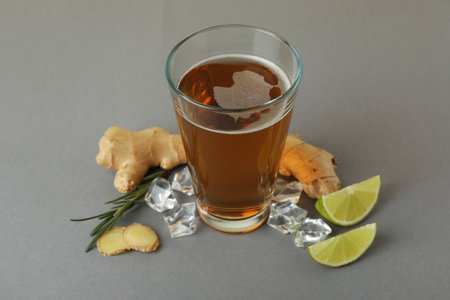 Glass of ginger beer and ingredients on gray background