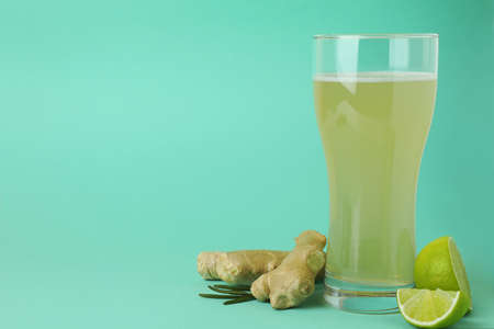 Glass of ginger beer and ingredients on mint background