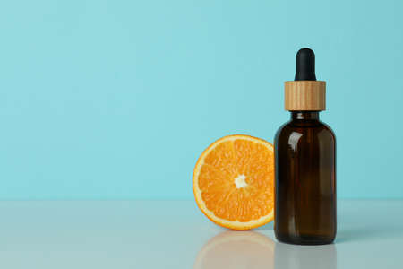 Dropper bottle with oil and orange against blue background