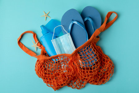 Bag with sea accessories, sunscreen and mask on blue background