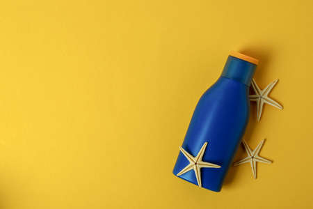 Blue bottle of sunscreen and starfishes on yellow background