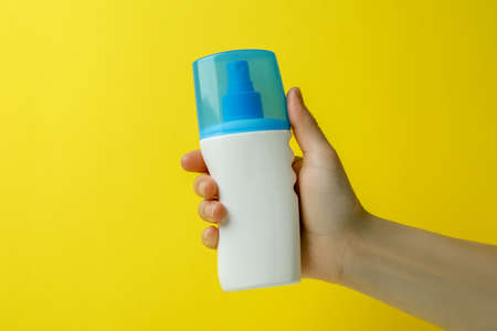 Female hand hold sunscreen on yellow backgroundの写真素材