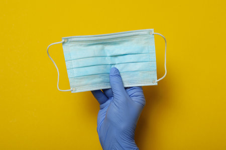 Hand in medical glove hold mask on yellow background