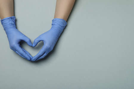 Hands in medical gloves shows heart on light gray background