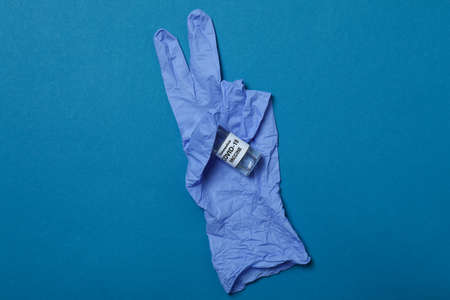 Medical glove with vaccine on blue background
