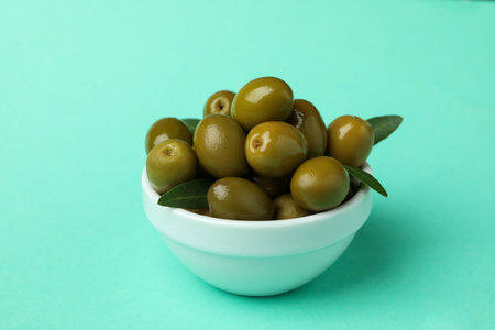 Bowl of green olives and leaves on mint backgroundの写真素材