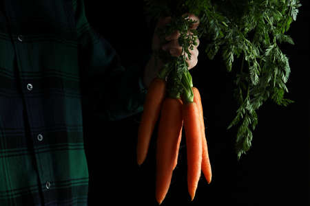 Woman hold fresh carrot on dark background