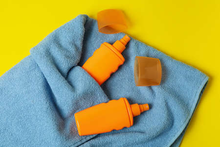 Bottles of sunscreen and towels on yellow background