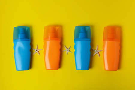 Bottles of sunscreen and starfishes on yellow background