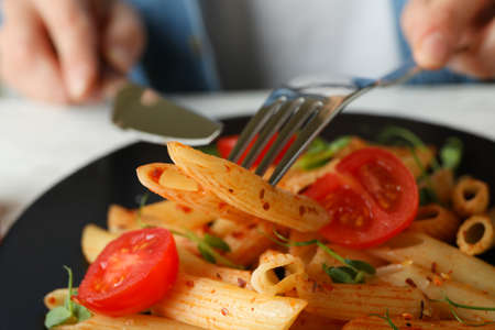 Concept of tasty eating with woman eats pasta with tomato sauce, close up