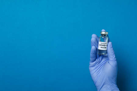 Hand in medical glove hold vaccine on blue background