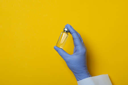 Hand in medical glove hold vaccine on yellow backgroundの写真素材