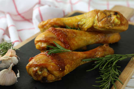 Board with roast chicken drumsticks, close up