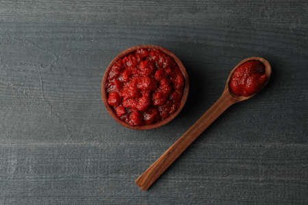 Wooden bowl and spoon with tomato paste on dark wooden background