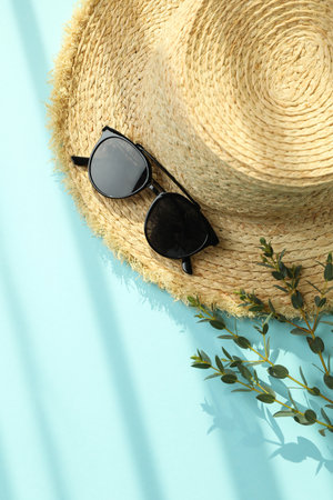 Straw hat, branch and sunglasses on blue background