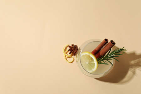 Glass of lemonade with cinnamon and rosemary on beige background