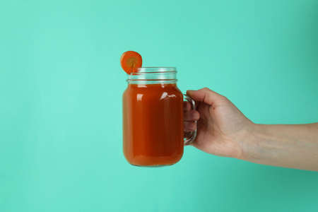Female hand hold jar of carrot juice on mint backgroundの写真素材