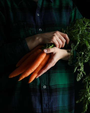 Woman hold fresh carrot against dark background
