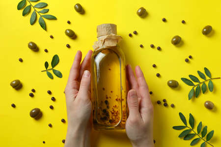 Female hands hold bottle of olive oil on yellow background