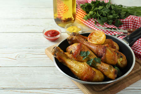 Concept of delicious eating with pan of roast chicken drumsticks on white wooden tableの写真素材
