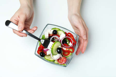 Female hands hold fork and bowl with greek saladの写真素材