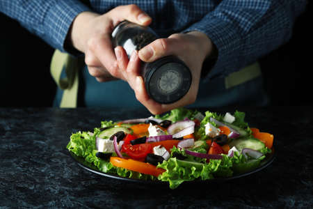 Woman grinding pepper on greek salad on black smokey tableの写真素材