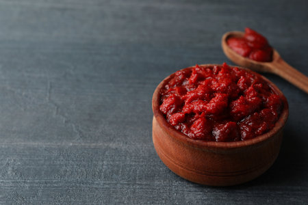 Wooden bowl and spoon with tomato paste on dark wooden backgroundの写真素材