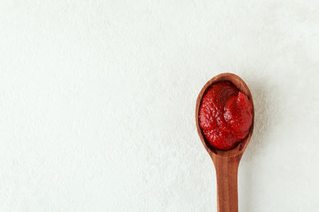 Wooden spoon with tomato paste on white textured backgroundの写真素材