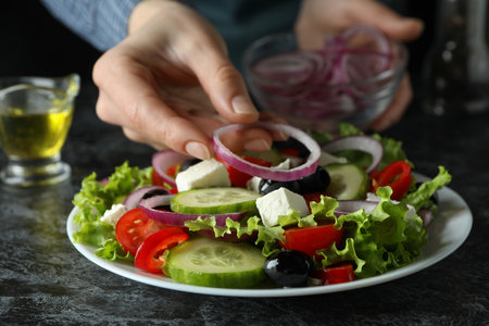 Woman put onions on greek salad on black smokey tableの写真素材