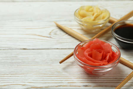 Pickled ginger, soy sauce and chopsticks on white wooden background