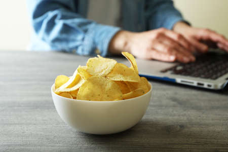 Bowl of potato chips against woman working on laptopの写真素材