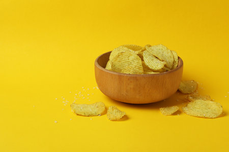 Bowl with potato chips on yellow background