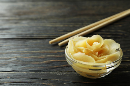 Bowl with pickled ginger and chopsticks on wooden backgroundの写真素材