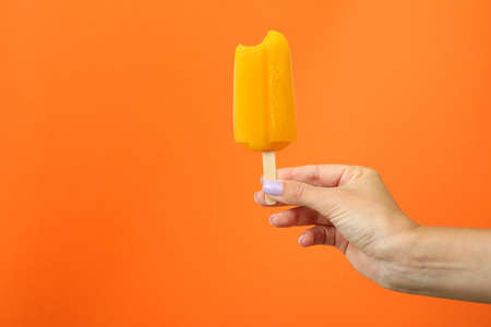 Female hand hold ice cream stick on orange backgroundの写真素材