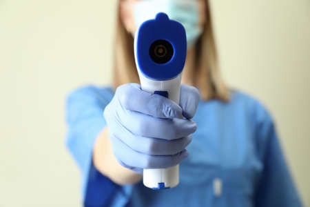 Female doctor holds thermometer gun, close up and front viewの写真素材