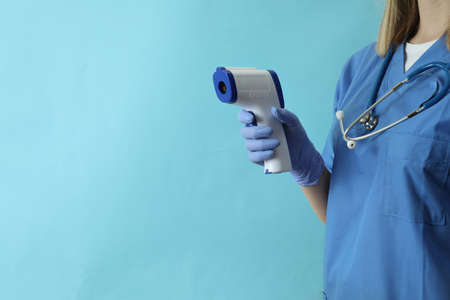 Female doctor hold thermometer gun on blue backgroundの写真素材