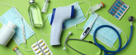 Medical tools and thermometer gun on green background