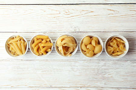 Bowls with uncooked pasta on white wooden backgroundの写真素材