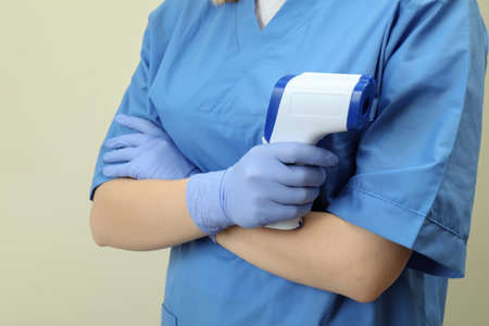 Female doctor hold thermometer gun on beige background