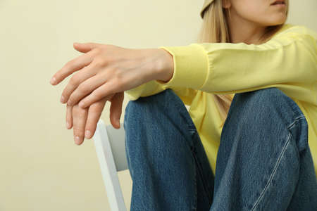 Young woman in yellow sweatshirt sitting against beige background