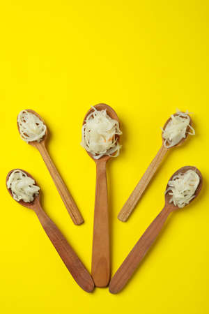 Wooden spoons with sauerkraut on yellow background