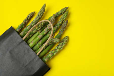 Bag with green asparagus on yellow background