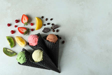 Black cones with ice cream and ingredients on white textured background