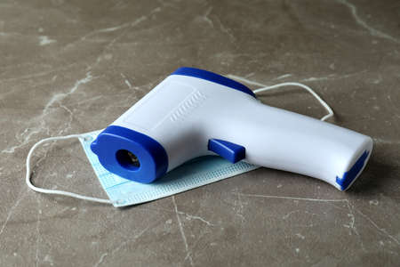Thermometer gun and medical mask on gray textured background