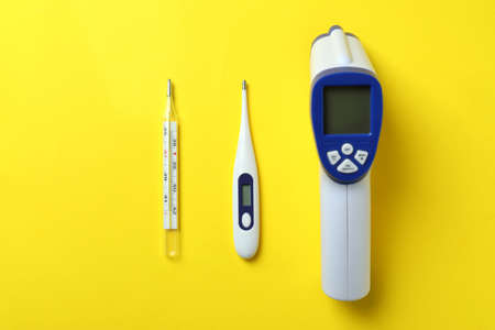 Different thermometers on yellow background, top view