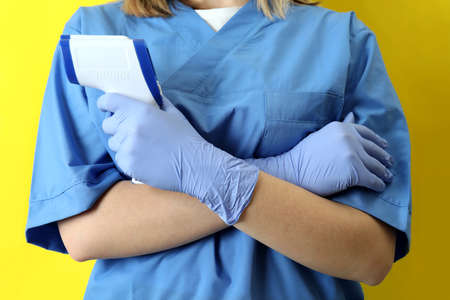 Female doctor hold thermometer gun on yellow backgroundの写真素材